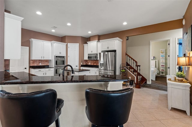 kitchen with a kitchen bar, sink, white cabinetry, kitchen peninsula, and stainless steel appliances