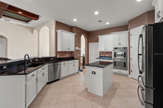 kitchen with sink, a center island, light tile patterned floors, stainless steel appliances, and white cabinets