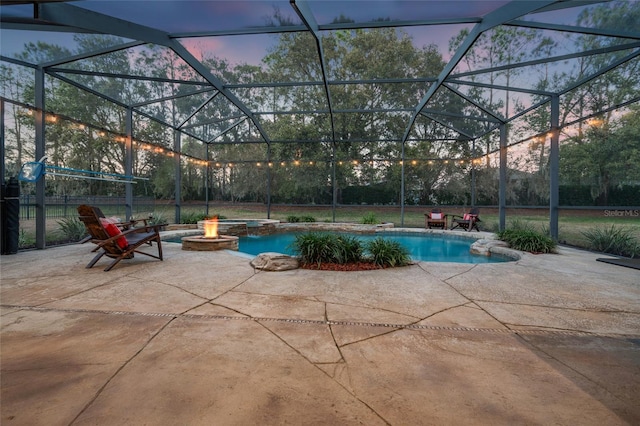 pool at dusk with a patio, glass enclosure, and an outdoor fire pit