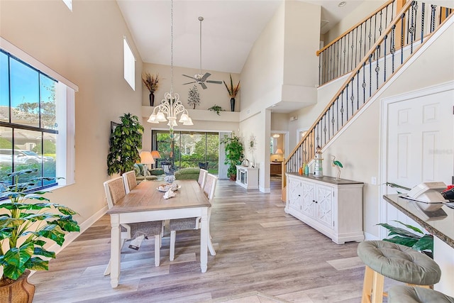 dining space featuring a towering ceiling, ceiling fan with notable chandelier, and light hardwood / wood-style flooring