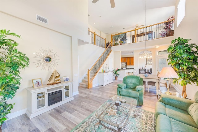 living room featuring a high ceiling, ceiling fan with notable chandelier, and light wood-type flooring