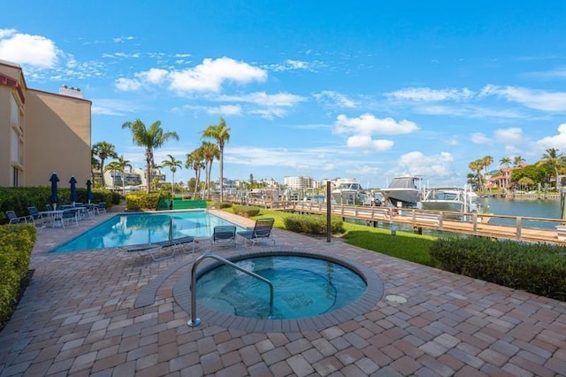 view of pool featuring a hot tub, a water view, and a patio area