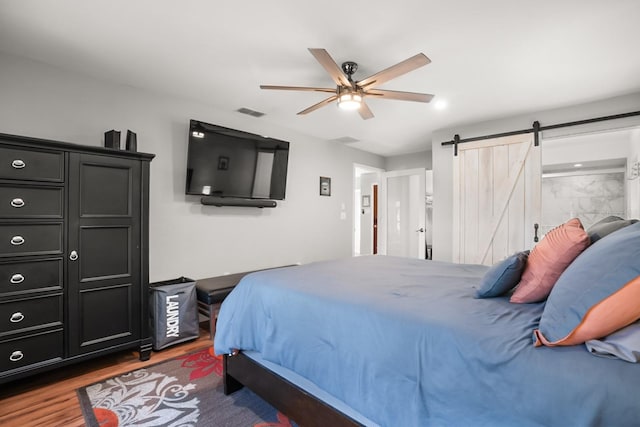 bedroom featuring a barn door, hardwood / wood-style floors, and ceiling fan