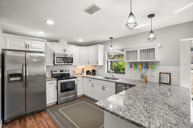 kitchen featuring sink, appliances with stainless steel finishes, kitchen peninsula, light stone countertops, and white cabinets