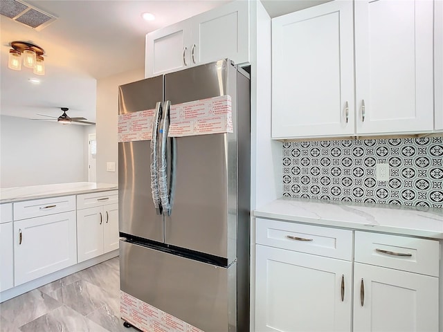 kitchen with white cabinetry, light stone counters, stainless steel fridge, and ceiling fan