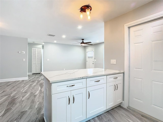 kitchen with light stone counters, ceiling fan, kitchen peninsula, and white cabinets