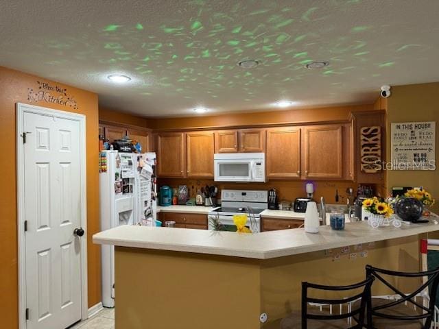 kitchen with light tile patterned flooring, a textured ceiling, a kitchen breakfast bar, kitchen peninsula, and white appliances