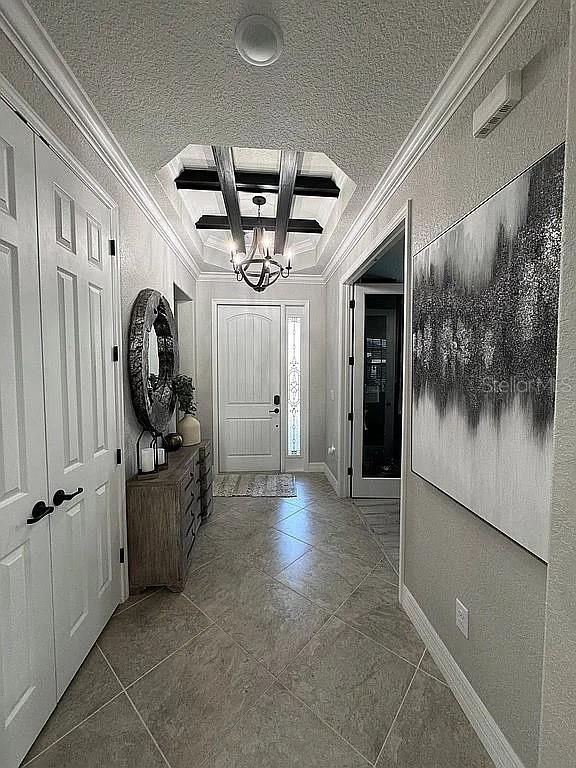 entrance foyer with crown molding, coffered ceiling, an inviting chandelier, and beam ceiling