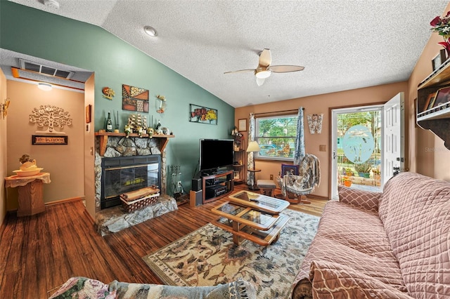 living room with lofted ceiling, a stone fireplace, wood-type flooring, a textured ceiling, and ceiling fan