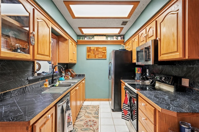 kitchen with sink, light tile patterned floors, stainless steel appliances, tasteful backsplash, and a textured ceiling