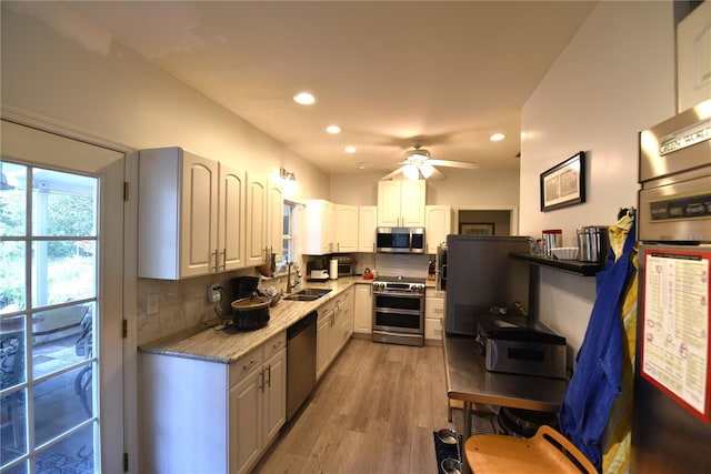 kitchen with sink, appliances with stainless steel finishes, white cabinetry, light hardwood / wood-style floors, and decorative backsplash