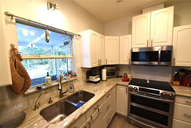 kitchen with white cabinetry, sink, light stone countertops, and appliances with stainless steel finishes