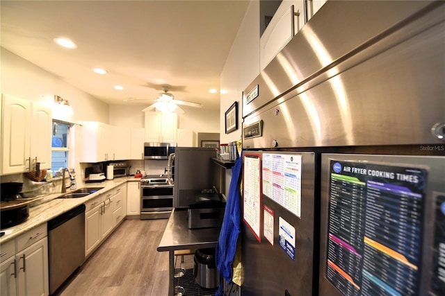 kitchen with white cabinetry, sink, ceiling fan, stainless steel appliances, and light wood-type flooring