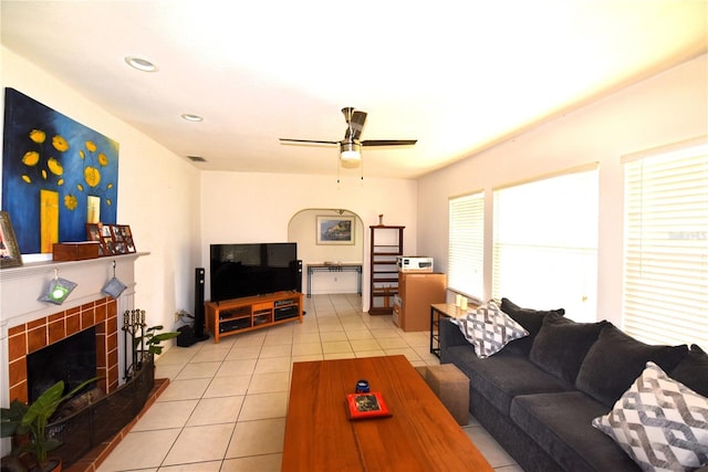 tiled living room with a tile fireplace and ceiling fan