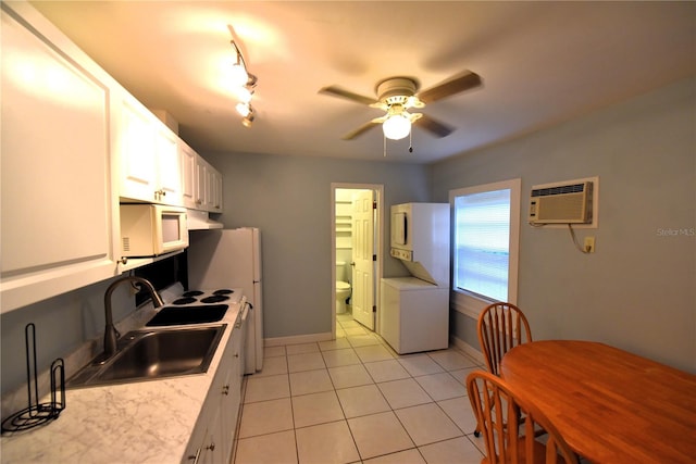 kitchen featuring stacked washer / drying machine, sink, white cabinetry, light tile patterned floors, and an AC wall unit