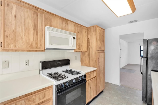 kitchen with white microwave, backsplash, freestanding refrigerator, light brown cabinetry, and gas stove