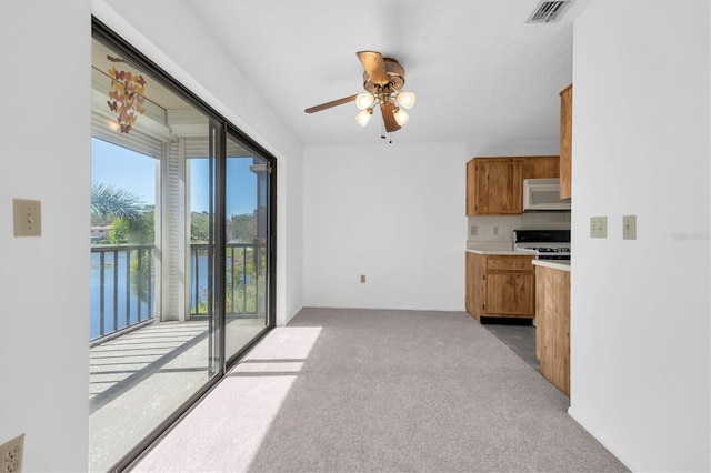 kitchen featuring white microwave, gas range oven, visible vents, and brown cabinetry