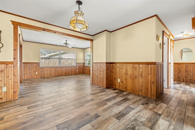 empty room with ceiling fan, ornamental molding, wooden walls, and hardwood / wood-style floors