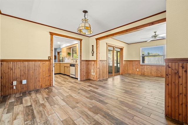 empty room with ceiling fan, ornamental molding, wooden walls, and light hardwood / wood-style flooring