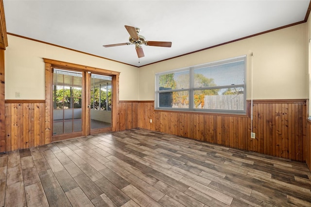 empty room featuring dark hardwood / wood-style flooring, ornamental molding, ceiling fan, and wood walls