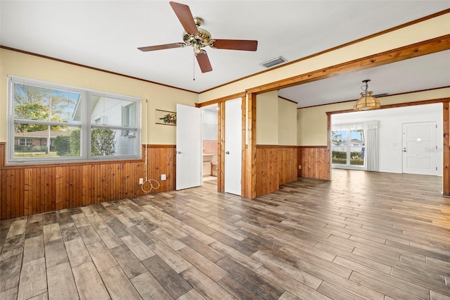 empty room featuring hardwood / wood-style floors, wooden walls, ornamental molding, and ceiling fan