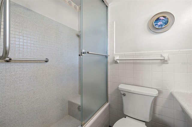 bathroom featuring enclosed tub / shower combo, tile walls, and toilet