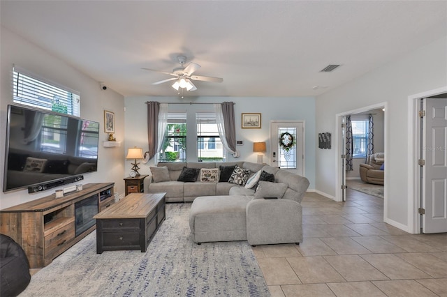 living area with healthy amount of natural light, a ceiling fan, light tile patterned floors, and baseboards