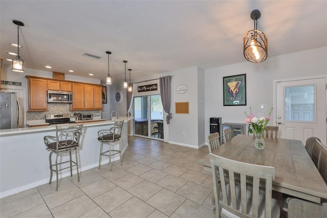 kitchen featuring stainless steel appliances, light tile patterned flooring, backsplash, light countertops, and brown cabinetry