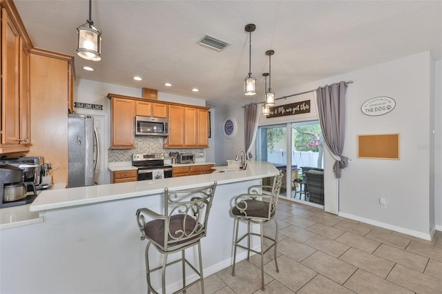 kitchen featuring stainless steel appliances, backsplash, a peninsula, a sink, and light countertops