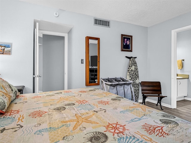 bedroom featuring hardwood / wood-style flooring, ensuite bath, and a textured ceiling