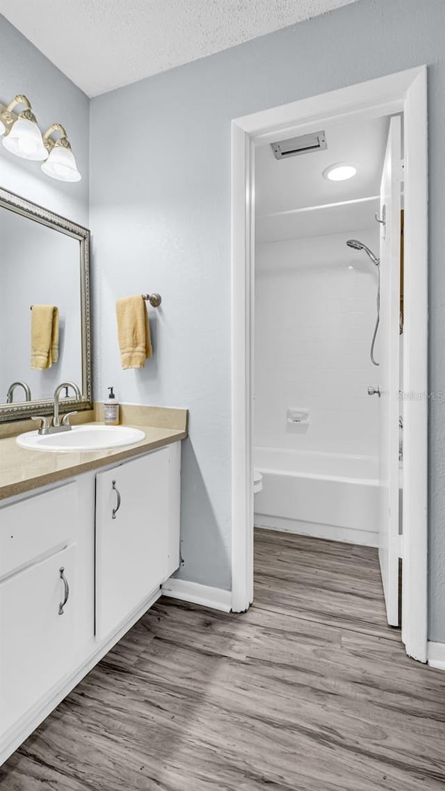 full bathroom featuring toilet, a textured ceiling, shower / bathtub combination, vanity, and hardwood / wood-style floors