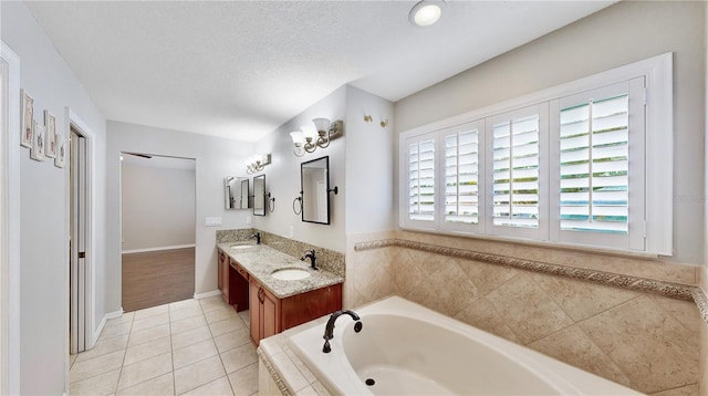 bathroom featuring tile patterned floors, tiled bath, vanity, and a textured ceiling