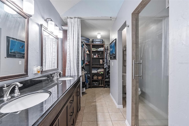 bathroom with vanity, a textured ceiling, a shower with shower door, tile patterned floors, and toilet