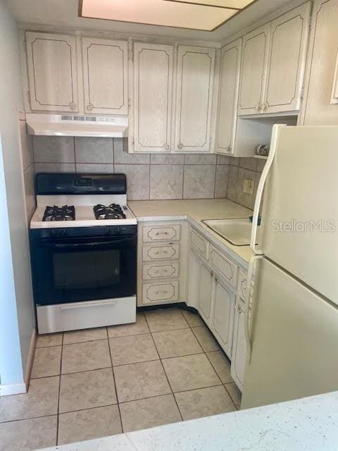 kitchen with sink, light tile patterned floors, white refrigerator, gas range oven, and decorative backsplash