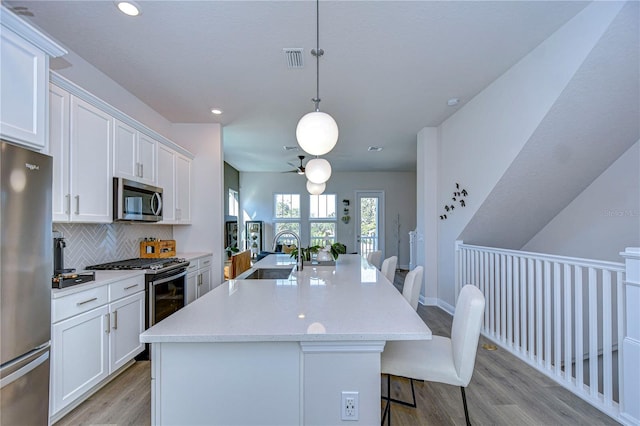 kitchen featuring pendant lighting, white cabinetry, a kitchen breakfast bar, stainless steel appliances, and a center island with sink