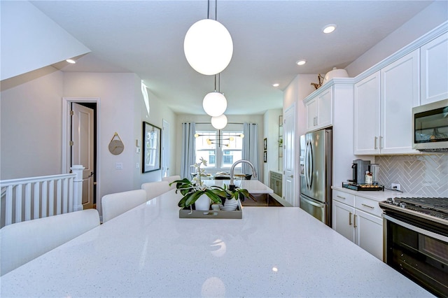 kitchen with appliances with stainless steel finishes, decorative light fixtures, tasteful backsplash, white cabinets, and light stone counters