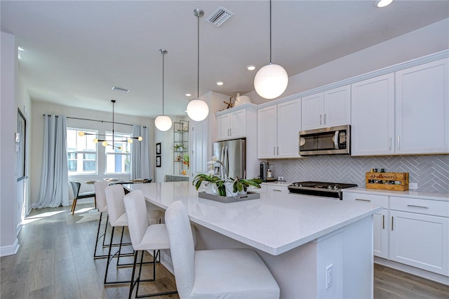 kitchen featuring stainless steel appliances, an island with sink, white cabinetry, and decorative light fixtures