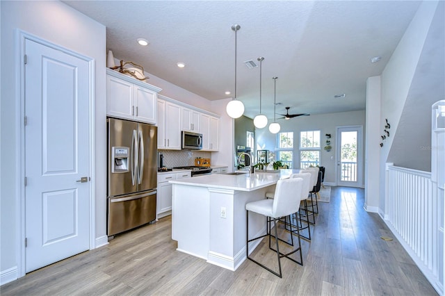 kitchen featuring decorative light fixtures, white cabinetry, a breakfast bar area, a kitchen island with sink, and stainless steel appliances