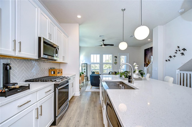 kitchen with light stone counters, hanging light fixtures, white cabinets, and appliances with stainless steel finishes