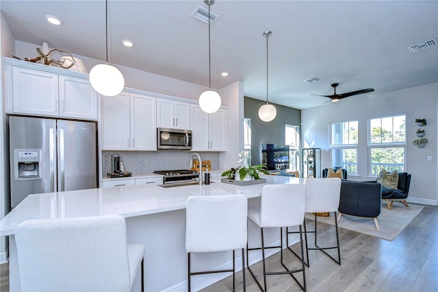 kitchen featuring white cabinetry, pendant lighting, stainless steel appliances, and a center island with sink