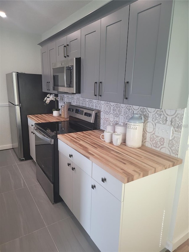 kitchen featuring gray cabinets, wooden counters, backsplash, tile patterned flooring, and stainless steel appliances