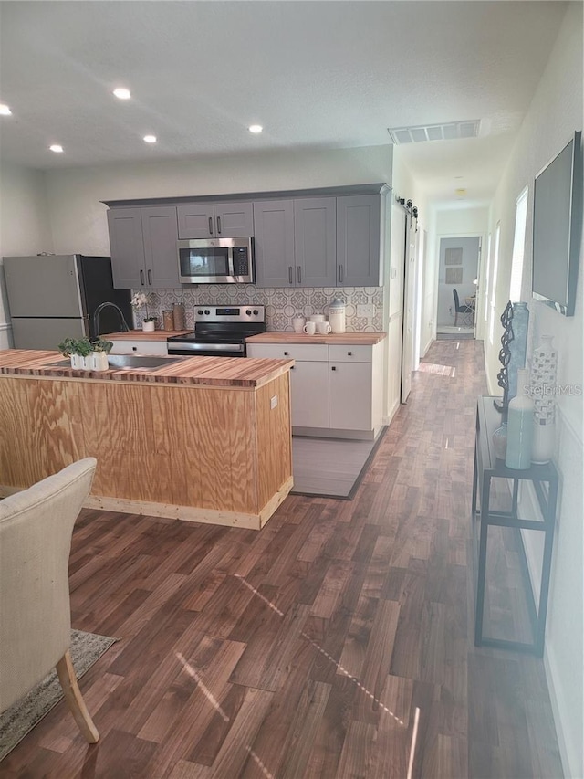 kitchen featuring appliances with stainless steel finishes, gray cabinetry, dark hardwood / wood-style flooring, decorative backsplash, and a barn door