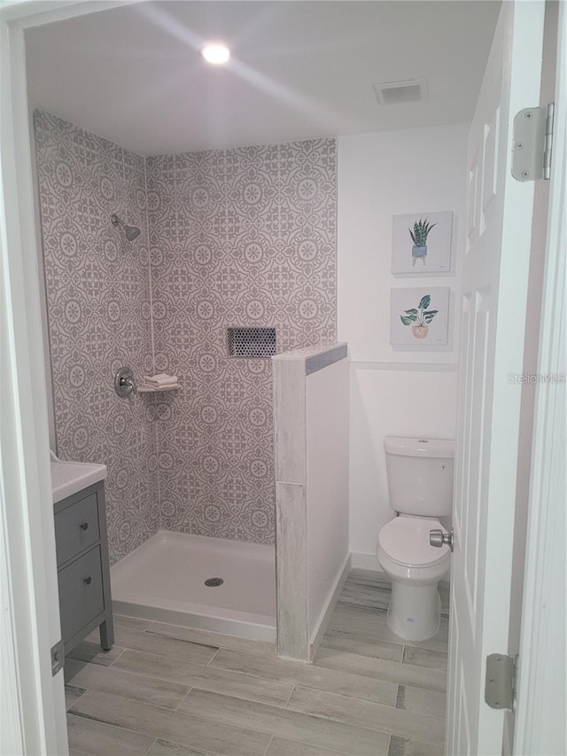 bathroom featuring vanity, a tile shower, and toilet