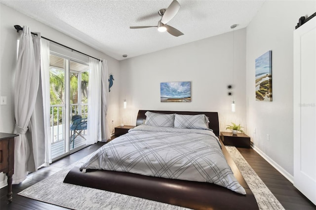 bedroom featuring a barn door, dark wood-type flooring, access to outside, and a textured ceiling