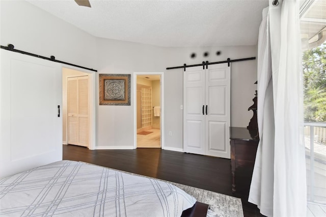 unfurnished bedroom with dark hardwood / wood-style flooring, connected bathroom, a barn door, and a textured ceiling