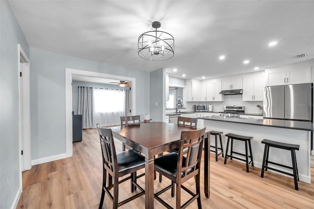 dining room featuring sink, ceiling fan with notable chandelier, and light hardwood / wood-style flooring