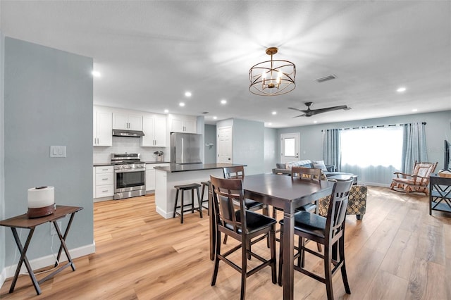 dining space with ceiling fan with notable chandelier and light hardwood / wood-style flooring