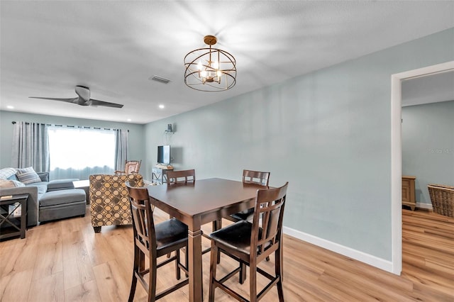 dining space with ceiling fan with notable chandelier and light hardwood / wood-style floors