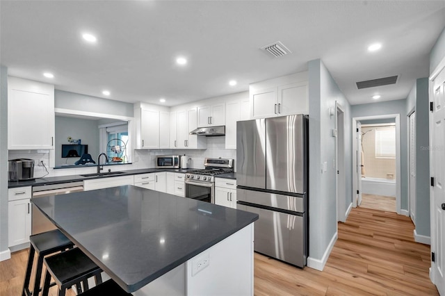 kitchen with a kitchen island, appliances with stainless steel finishes, sink, white cabinets, and a kitchen bar