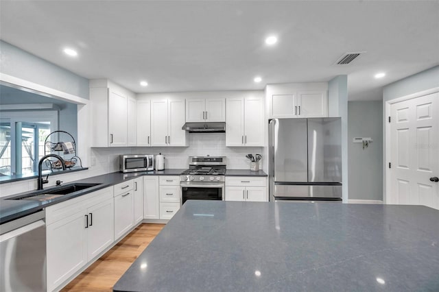 kitchen featuring sink, stainless steel appliances, light hardwood / wood-style floors, white cabinets, and decorative backsplash